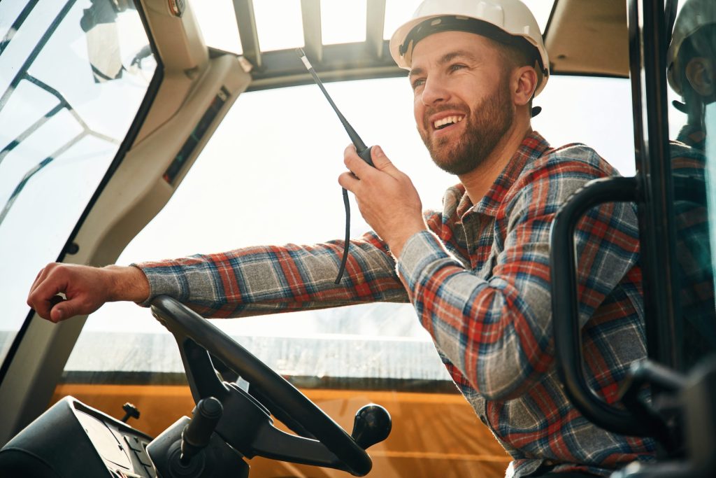 Construction worker using two-way radio inside vehicle cabin- Rough Terrain Forklift Certification