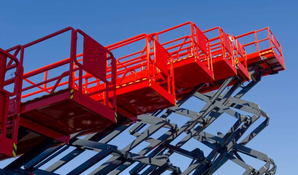 Red scissor lift platforms with safety railings extended upward against blue sky